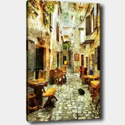 Lerretsbilder|Lerretsbilder-Lerretsbilde 70x100 cm - Pittoresk smug med trebord og stoler, omgitt av gamle steinhus Flerfärgad